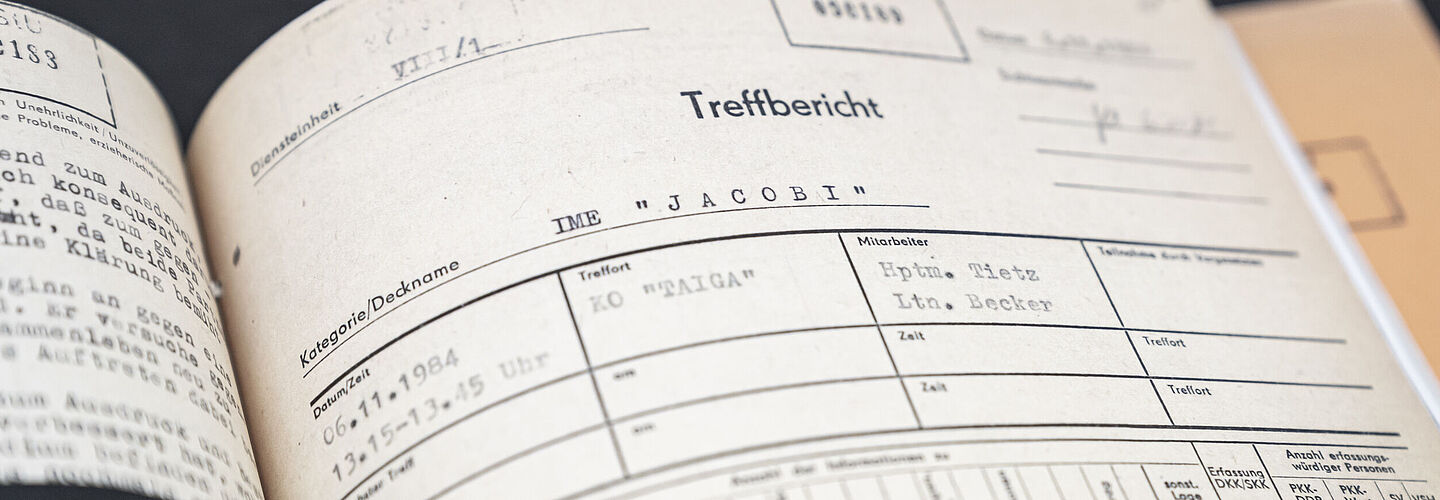 Blick in die aufgeschlagene Beispielakte zum Inoffiziellen Mitarbeiter "Knut Jacobi". Zu sehen ist ein Formblatt zu einem Treff des Inoffiziellen Mitarbeiters mit zwei Stasi-Offizieren.