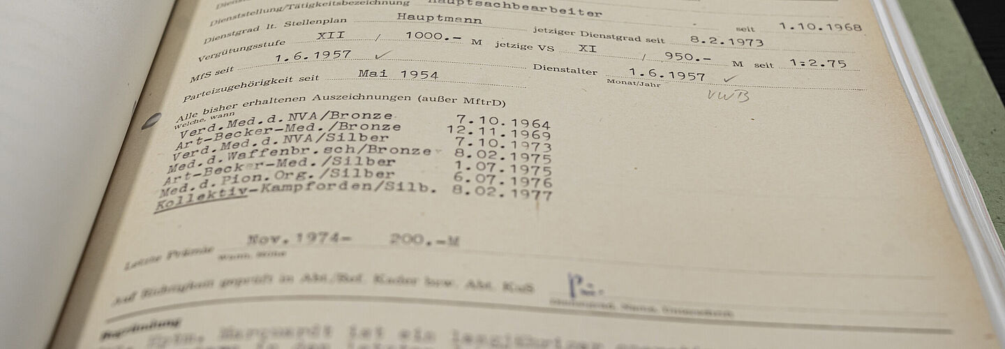 Ein Blick in eine aufgeschlagene Akte. Zu sehen sind Informationen zur Anstellung Willi Marquardts bei der Stasi sowie Gehalts und Auszeichnungsnachweise